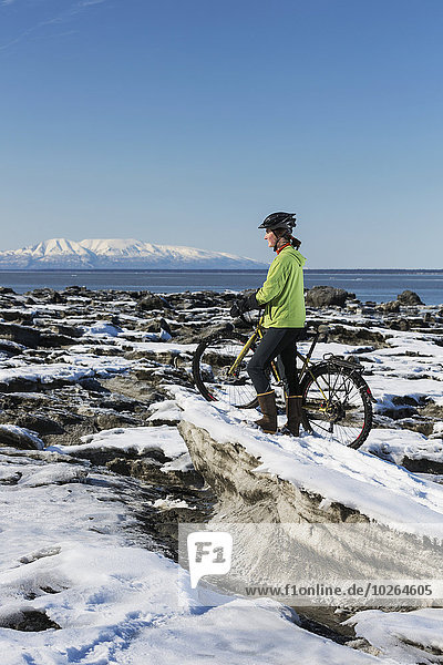 Young woman with her bicycle stands on frozen ice chunks along the Tony Knowles Coastal Trail  Anchorage  Southcentral Alaska