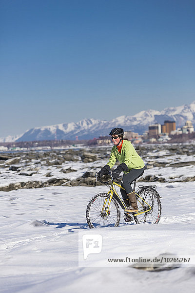 A young woman rides a studded tire bicycle next to the Tony Knowles Coastal Trail  Anchorage  Southcentral Alaska  USA.