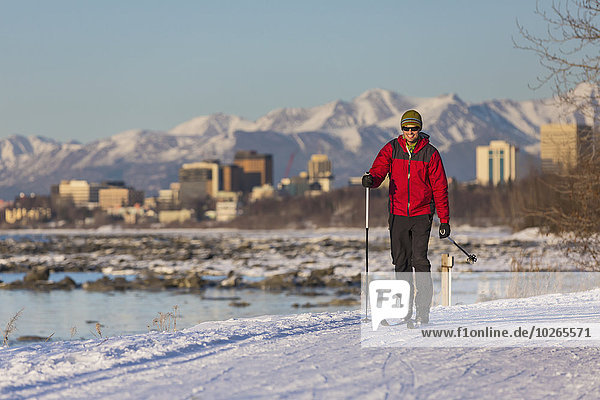 Man cross country skiing on the Tony Knowles Coastal Trail near Earthquake Park with Anchorage skyline in the background  Cook Inlet  Southcentral Alaska