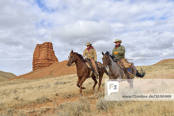 Cowboy and Cowgirl Riding Horses with Castel Rock in the background  Shell  Wyoming  USA