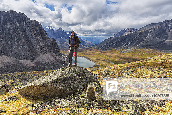 Man standing on a rock overlooking the granite peaks of Tombstone Territorial Park in autumn; Yukon  Canada