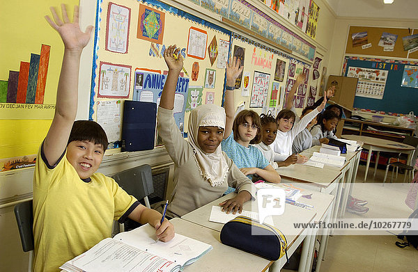 Grade 5 students raising their hands at their desks in the classroom