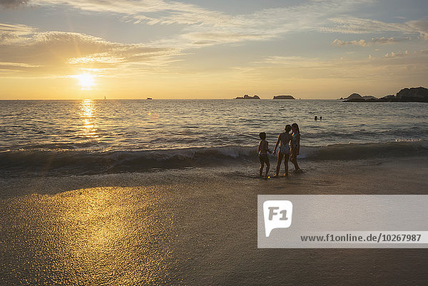 Children standing at the water's edge at sunset; Ixtapa-Zihuatanejo  Guerrero  Mexico