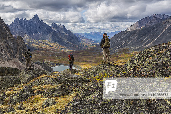 A group of hikers standing on rocks overlooking the colourful valleys in Tombstone Territorial Park in autumn; Yukon  Canada