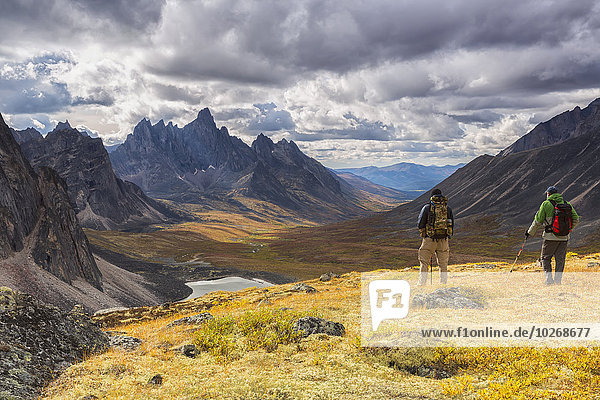 Hikers on an overlook viewing the beautiful autumn colours in Tombstone Territorial Park  with Tombstone Mountain in the distance; Yukon  Canada