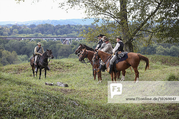 Five American Civil War confederate re-enactors sitting on horses and discussing the battle with a railroad bridge in the background; United States of America
