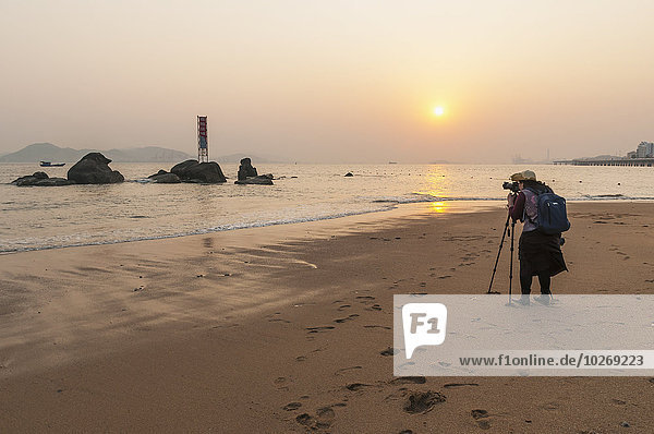 A young woman taking a picture on the beach at sunset; Xiamen  Fujian Province  China
