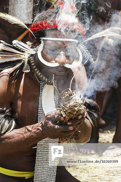 Dani men wearing an elaborate headdress of bird of paradise or cassowary feathers lighting a fire  Obia Village  Baliem Valley  Central Highlands of Western New Guinea  Papua  Indonesia