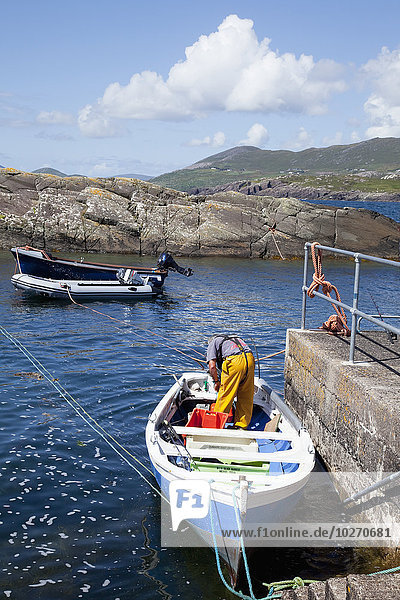 A man stands in his boat by the pier preparing for fishing  near Caherdaniel; County Kerry  Ireland