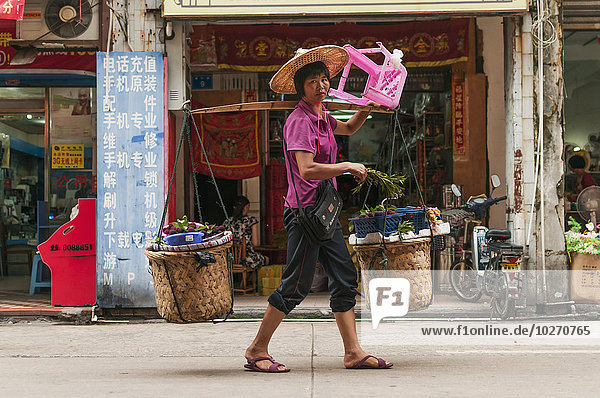 Eine Frau trägt ihre Einkäufe mit dem typischen Bambusstock  der in China sehr verbreitet ist; Xiamen  Provinz Fujian  China