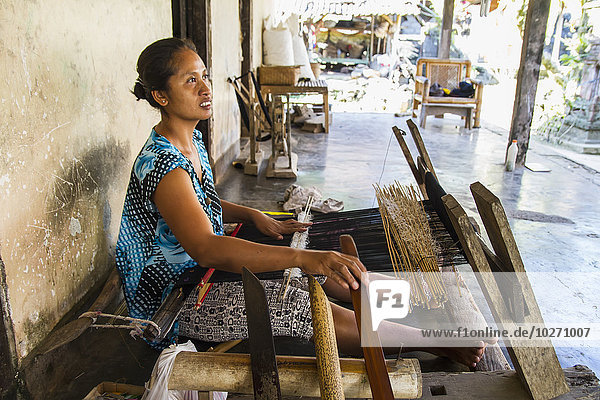 Weberin bei der Herstellung eines Songket-Textils mit zusätzlichen Schussmustern auf einem Webstuhl mit Rückengurt  Sidemen  Bali  Indonesien