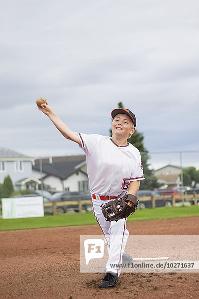 Ein kleiner Junge wirft den Baseball vom Pitchers Mound während eines Ballspiels in einer weißen Uniform mit einem Baseball und Handschuh; Fort McMurray  Alberta  Kanada'.