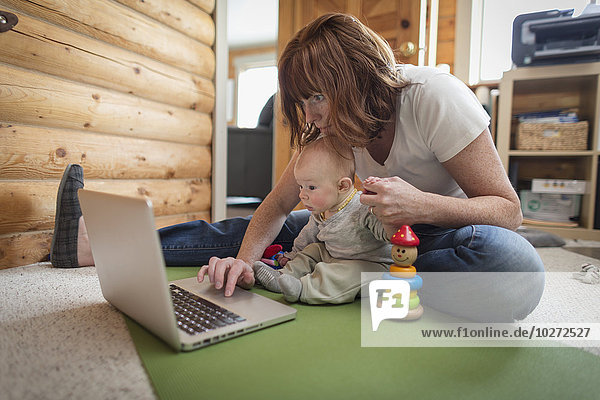 Mother and baby sitting in front of a laptop on the floor of a cabin  Homer  Southcentral Alaska