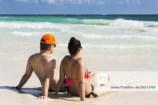 'Couple laying and sitting on sandy beach with waves coming in and blue sky; Tulum  Quintana Roo  Mexico'