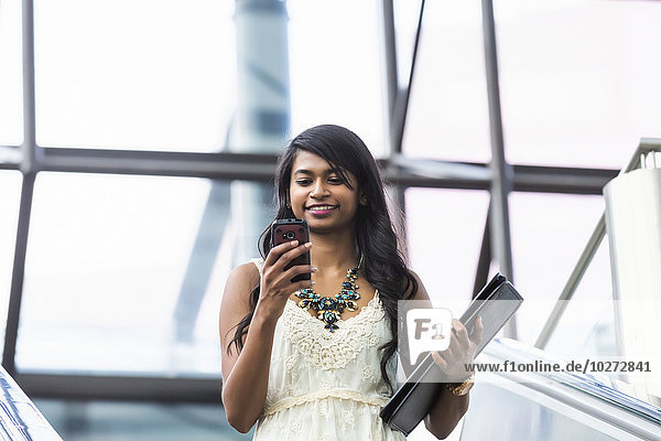 Junge Geschäftsfrau  die auf der Rolltreppe eine SMS auf ihrem Smartphone schreibt; Edmonton  Alberta  Kanada'.