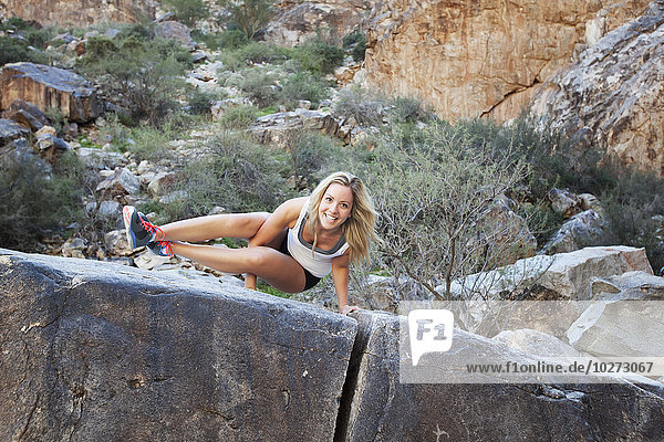 'A young woman doing a difficult yoga pose on a large rock in White Tank Mountain range; Arizona  United States of America'