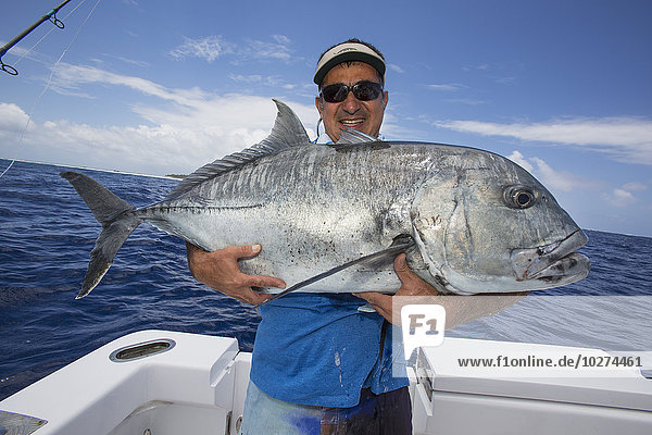 'Fisherman holding a fresh caught Giant Trevally fish; Tahiti'