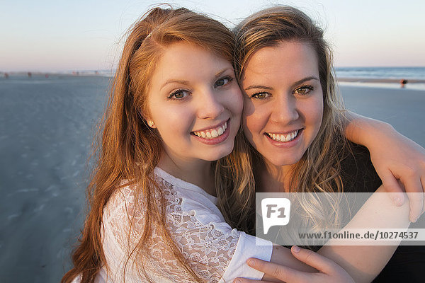 Zwei junge Frauen posieren am Strand in einer Umarmung bei Sonnenuntergang; Vereinigte Staaten von Amerika'.