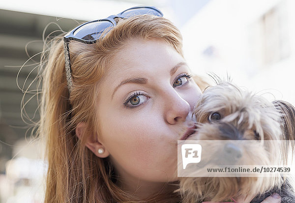 'Red haired young woman holding and kissing her small dog; United States of America'