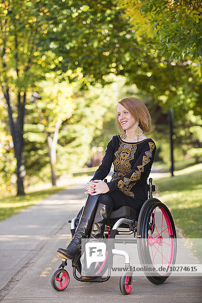 Junge querschnittsgelähmte Frau in ihrem Rollstuhl auf einem Weg in einem Stadtpark im Herbst; Edmonton  Alberta  Kanada'.