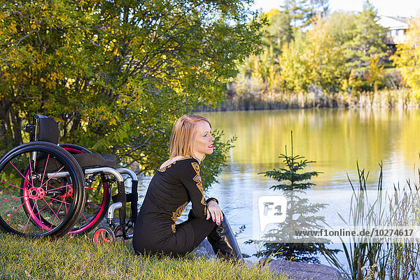 Junge querschnittsgelähmte Frau neben ihrem Rollstuhl am Wasser in einem Stadtpark im Herbst; Edmonton  Alberta  Kanada'.
