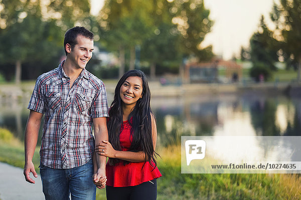 Gemischtrassiges Paar  das Zeit miteinander verbringt und im Herbst um einen See in einem Park spaziert; St. Albert  Alberta  Kanada'.