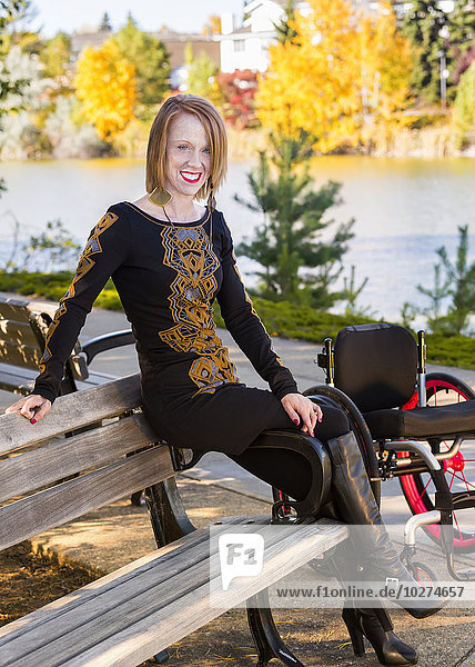 'Young disabled woman out of her wheelchair sitting on a bench in a city park in autumn; Edmonton  Alberta  Canada'