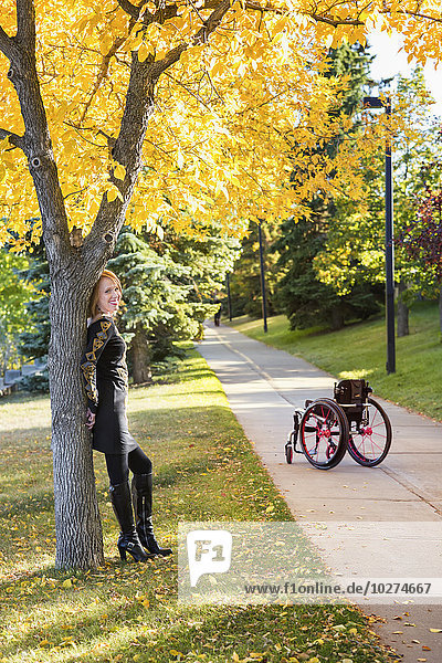Junge querschnittsgelähmte Frau  die ohne ihren Rollstuhl auf einem Weg in einem Stadtpark im Herbst an einem Baum steht; Edmonton  Alberta  Kanada'.