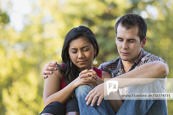 'Mixed race couple praying together in a park in autumn; St. Albert  Alberta  Canada'