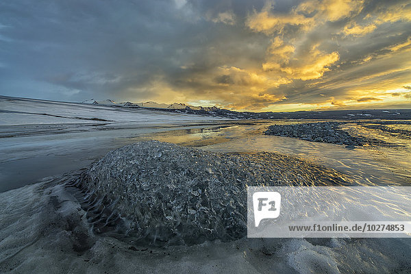 Der Sonnenaufgang erhellt den Himmel über einem zu einem Fluss gefrorenen Eisberg an der Südküste Islands; Island