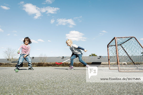 Kinder spielen Hockey auf dem Hof gegen den blauen Himmel