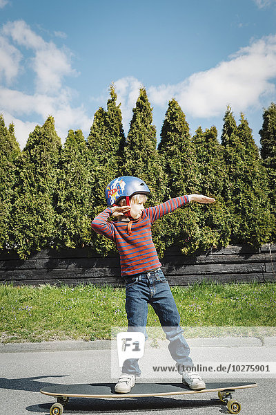 Volle Länge des Jungen  der auf dem Skateboard auf dem Hof steht.