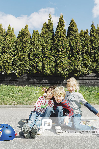 Porträt von glücklichen Jungen und Mädchen auf dem Skateboard gegen Bäume