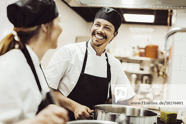Happy male chef looking at colleague while cooking in kitchen