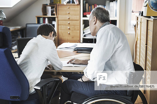 Behinderter Mann  der dem Sohn hilft  zu Hause zu studieren.