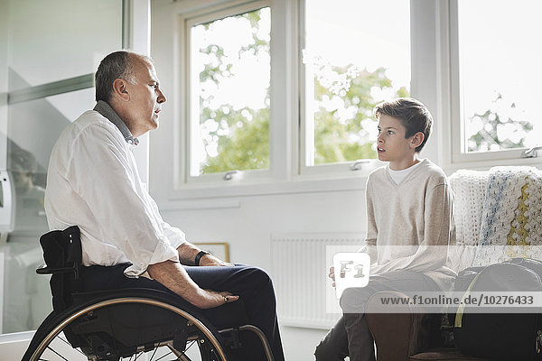 Behinderter Vater im Rollstuhl im Gespräch mit dem Sohn zu Hause