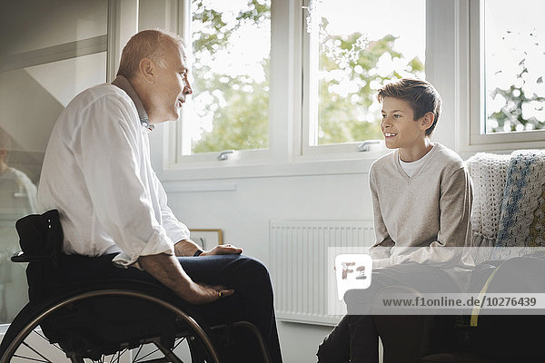 Behinderter Mann im Rollstuhl im Gespräch mit dem Sohn zu Hause