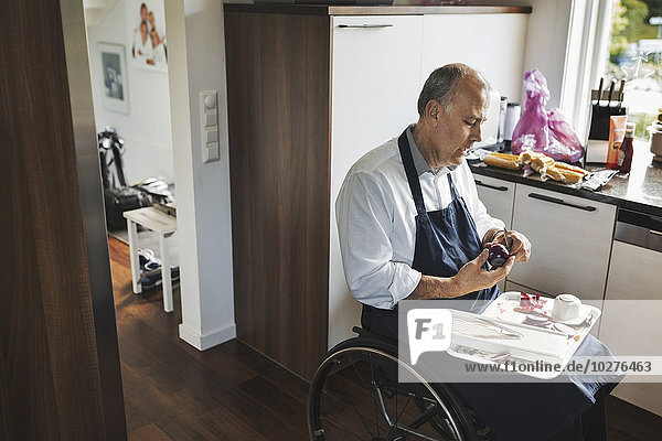 Behinderter Mann im Rollstuhl beim Zwiebelschneiden in der Küche