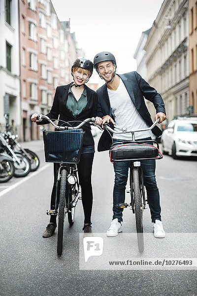 Portrait of happy business people with bicycles standing on city street