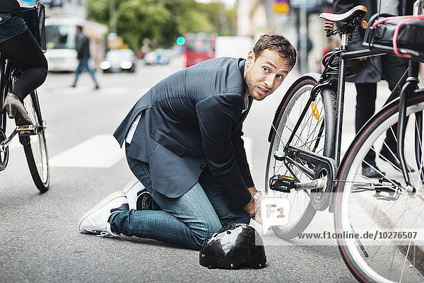 Geschäftsmann schaut weg  während er das Fahrrad auf der Straße repariert.