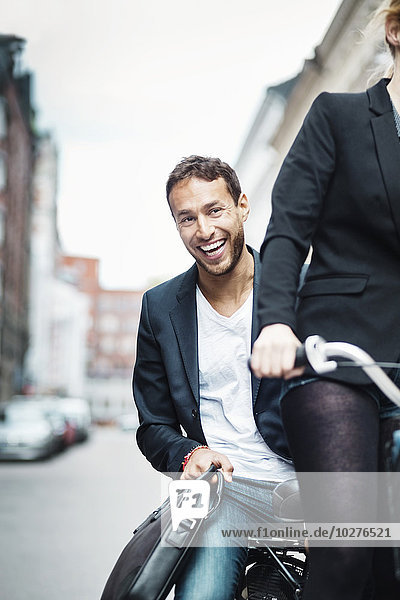 Porträt eines glücklichen Geschäftsmannes  der mit seinem Kollegen auf der Straße Fahrrad fährt.