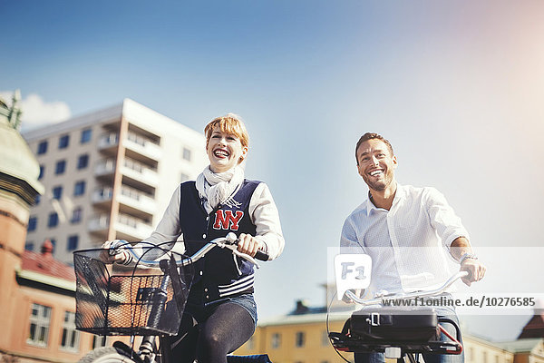 Glückliche Geschäftsleute auf Fahrrädern in der Stadt gegen den blauen Himmel