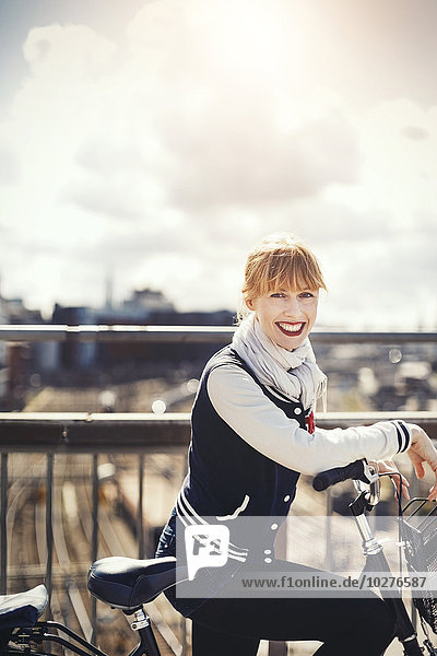 Seitenansicht Porträt einer glücklichen Geschäftsfrau  die mit dem Fahrrad auf der Brücke gegen den Himmel steht