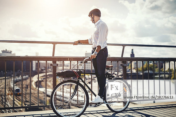 Geschäftsmann mit Blick auf die Stadt im Stehen auf dem Fahrrad