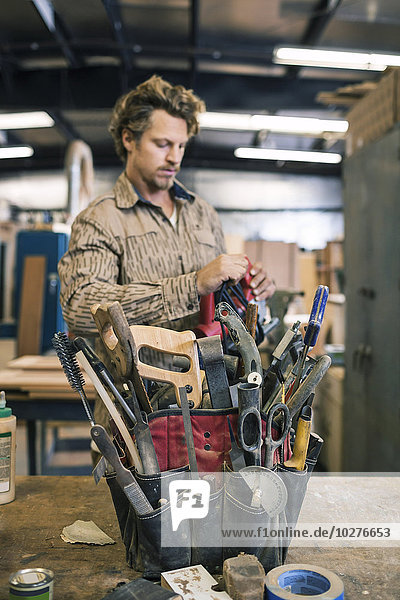 Carpenter standing by tool belt on table in workshop