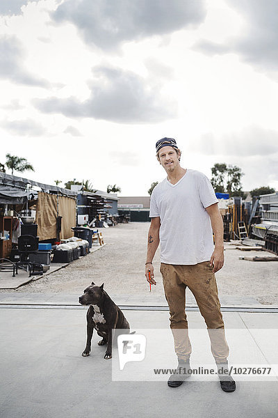 Portrait of carpenter standing with dog outside workshop against sky