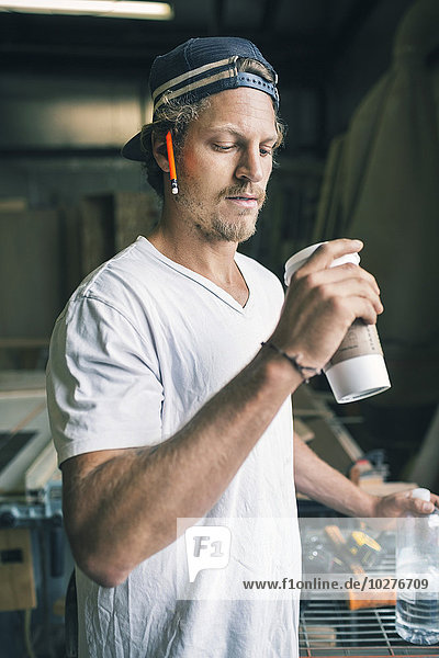 Carpenter holding disposable coffee cup and water bottle in workshop