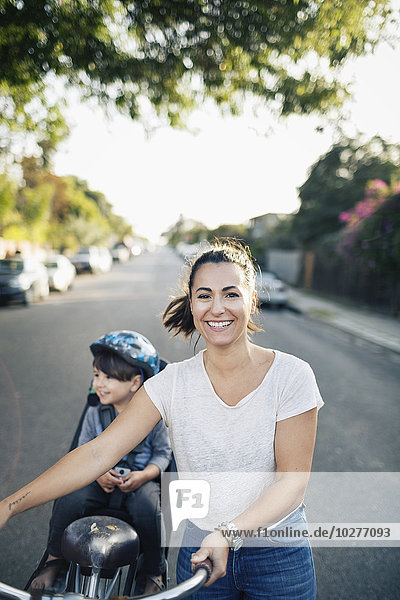 Portrait of happy woman holding bicycle with son sitting on back seat