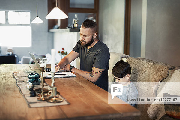 Mann schreibt im Buch  während der Sohn am Esstisch sitzt.