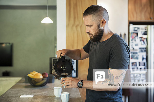 Mann gießt Kaffee in die Tasse in der Küche zu Hause